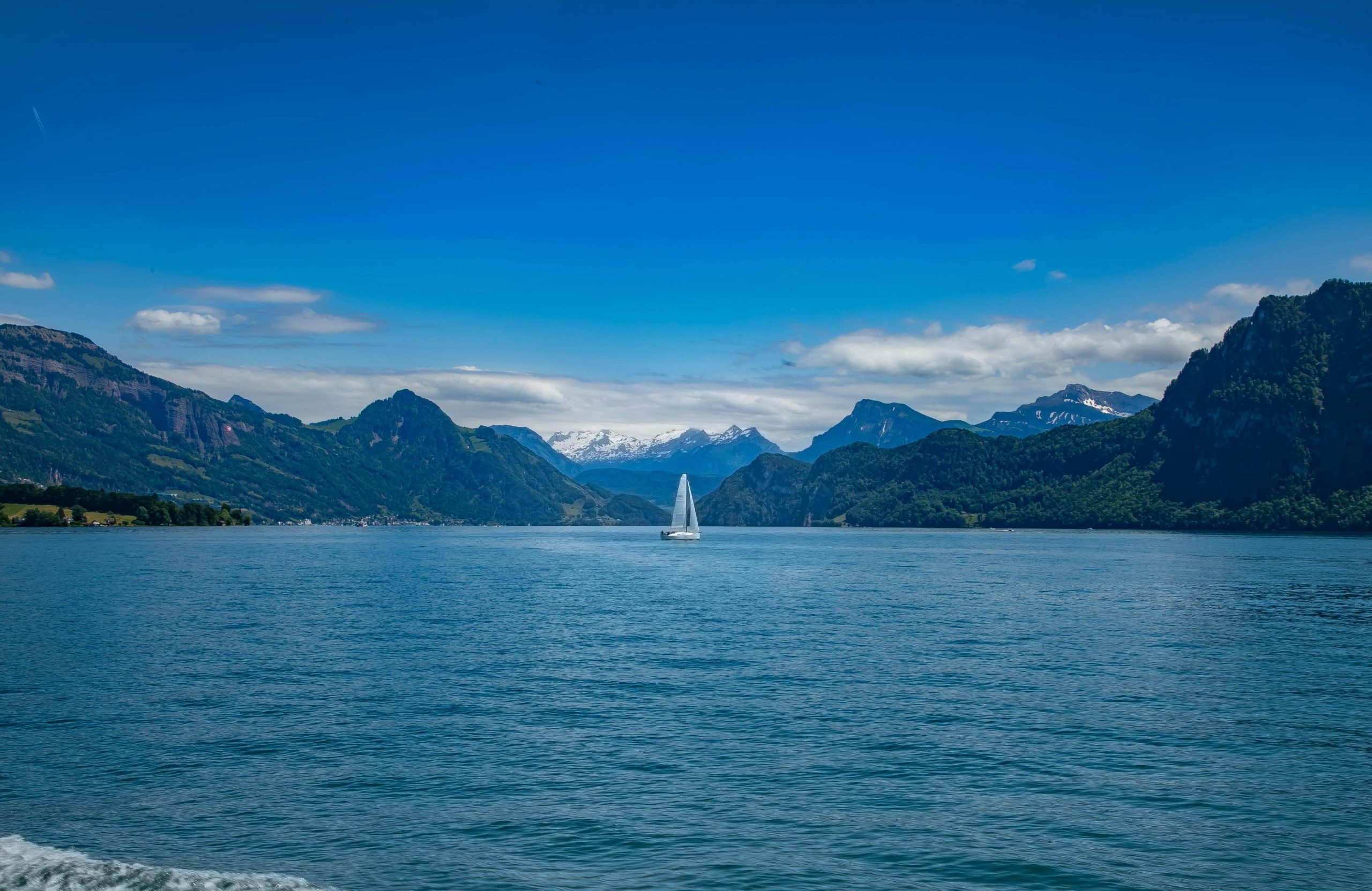 Blauer See mit einem Segelboot und Bergen im Hintergrund